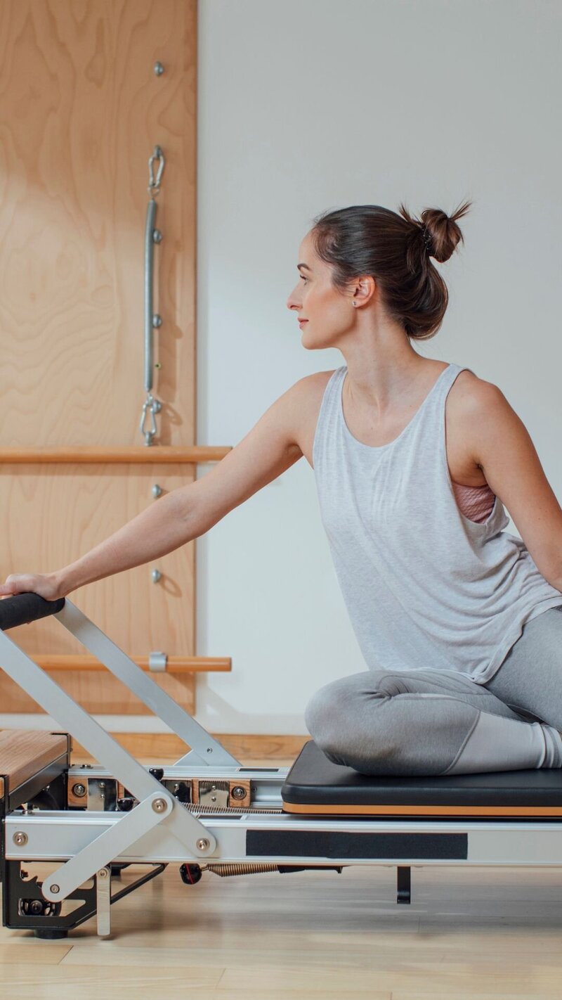 A woman hunched over a piece of pilates equipment with her hands on one step and her feet on a lower step.